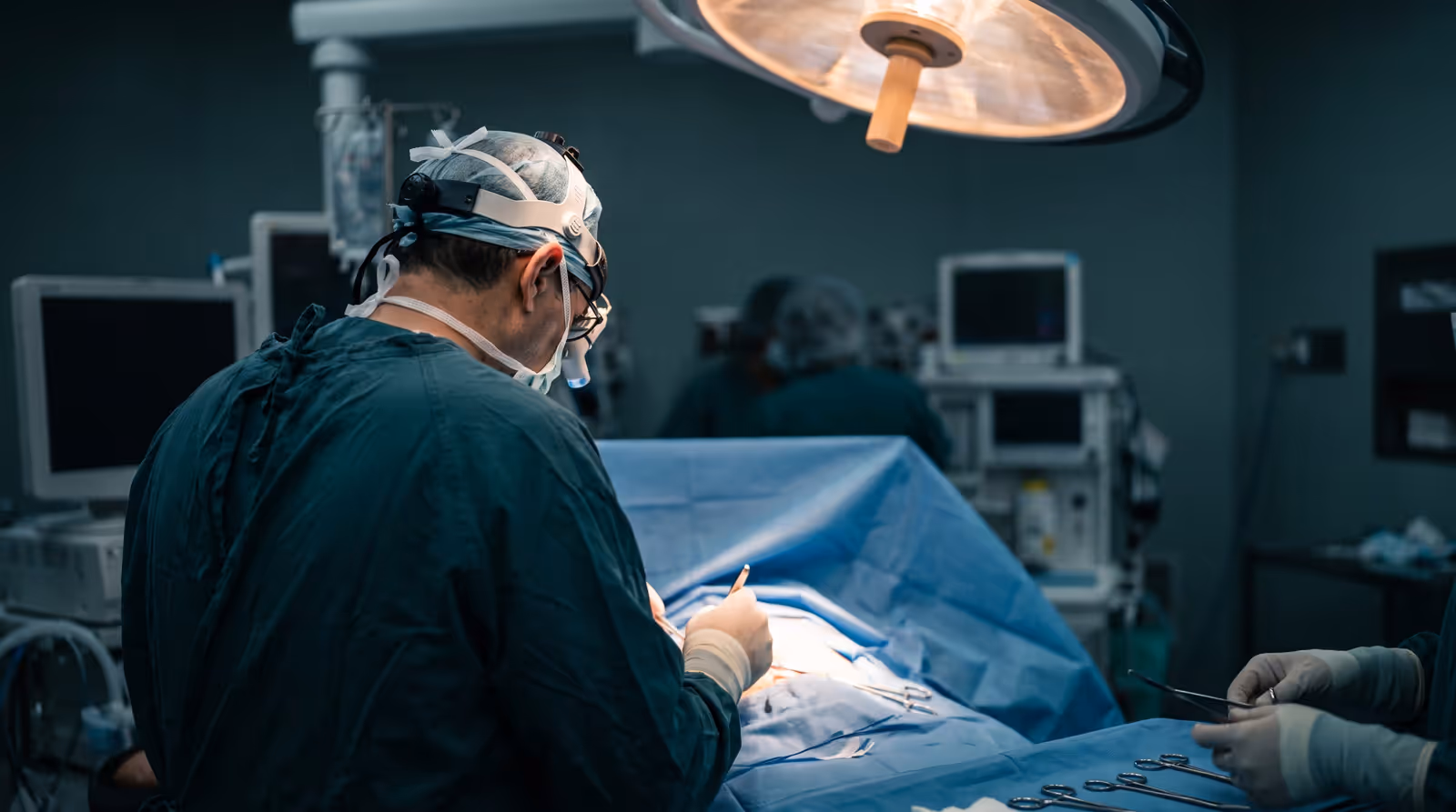 Vascular surgeon in scrubs and surgical loupes working over a sterile draped field in an operating room